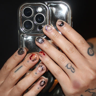 Close-up of hands with tattoos and painted nails holding a reflective phone case.